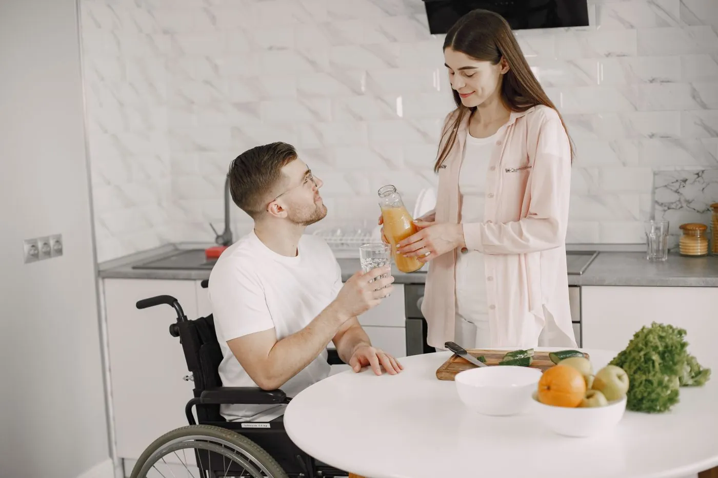 Muž na vozíku s pomocnicí v moderní kuchyni