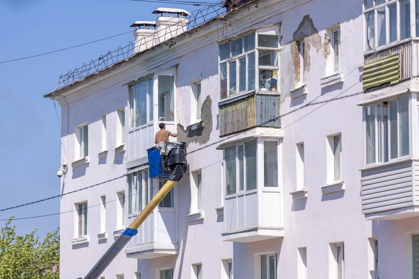 Dělník na plošině opravuje fasádu panelového domu
